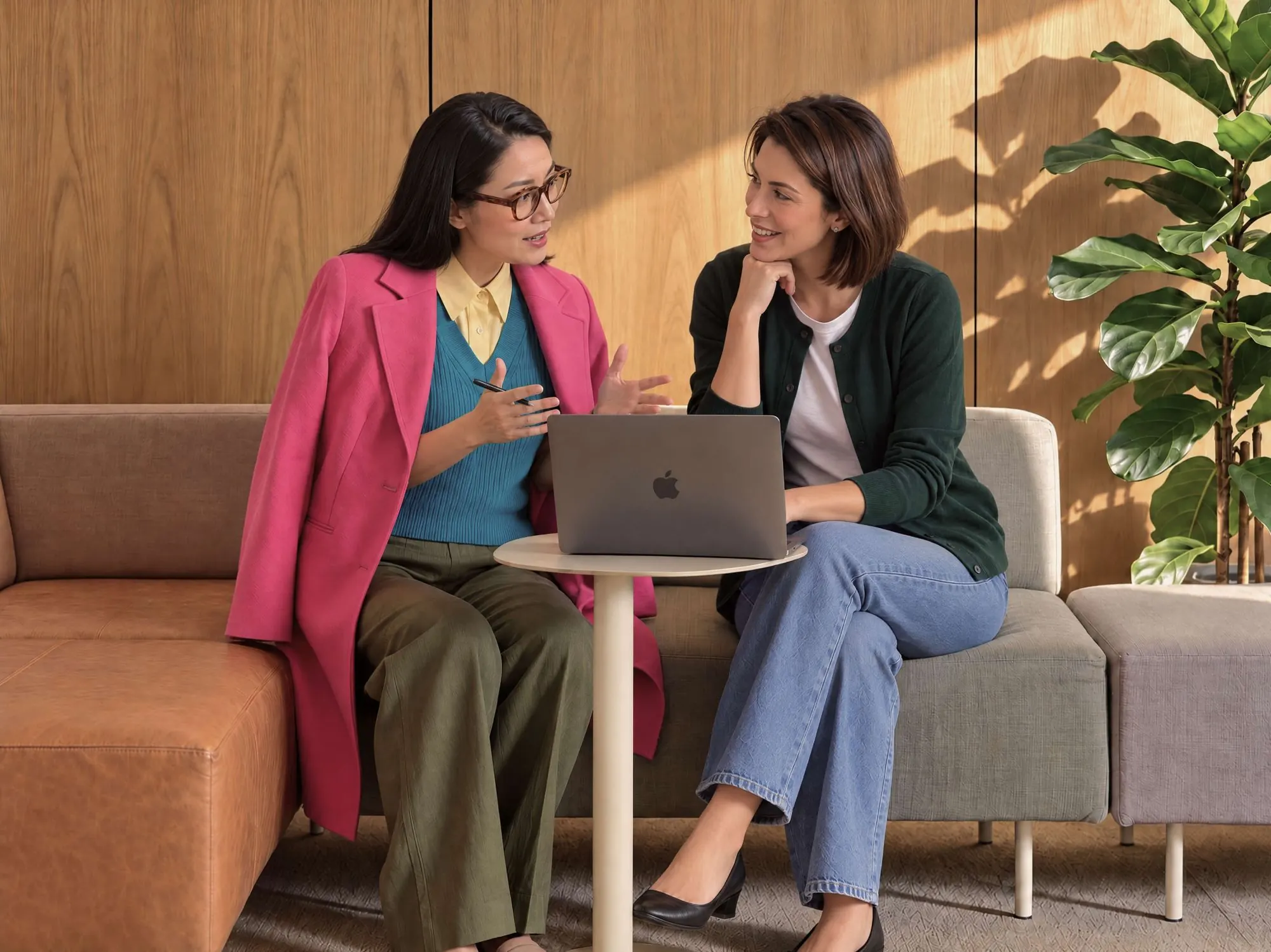 Two colleagues on a sofa talking through work on a laptop