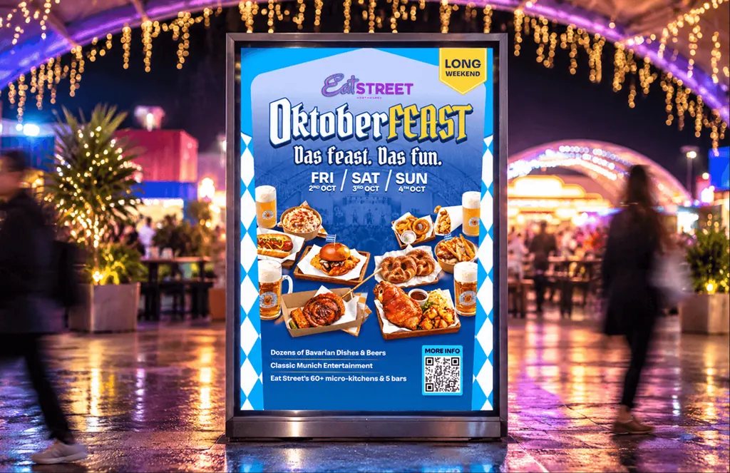Eat Street Oktoberfeast poster on a stand at a night market under festoon lights, with Bavarian food and beer