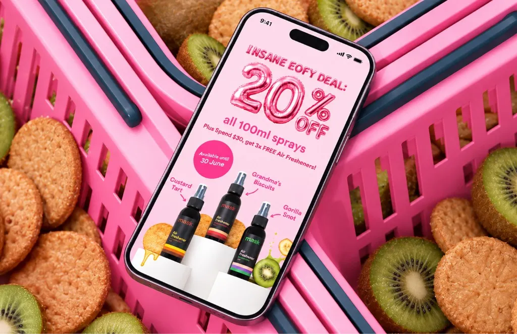 Phone in a pink shopping basket showing MaskCo’s EOFY deal, 20% off all 100ml sprays, among biscuits and kiwi fruit