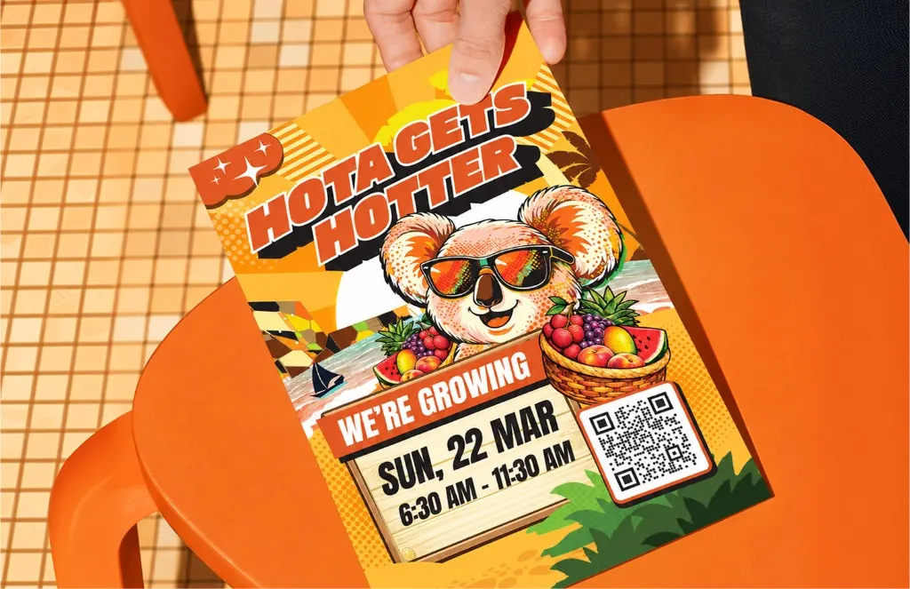 Hand holding a HOTA Gets Hotter flyer of a koala in sunglasses with a fruit basket, over an orange stool