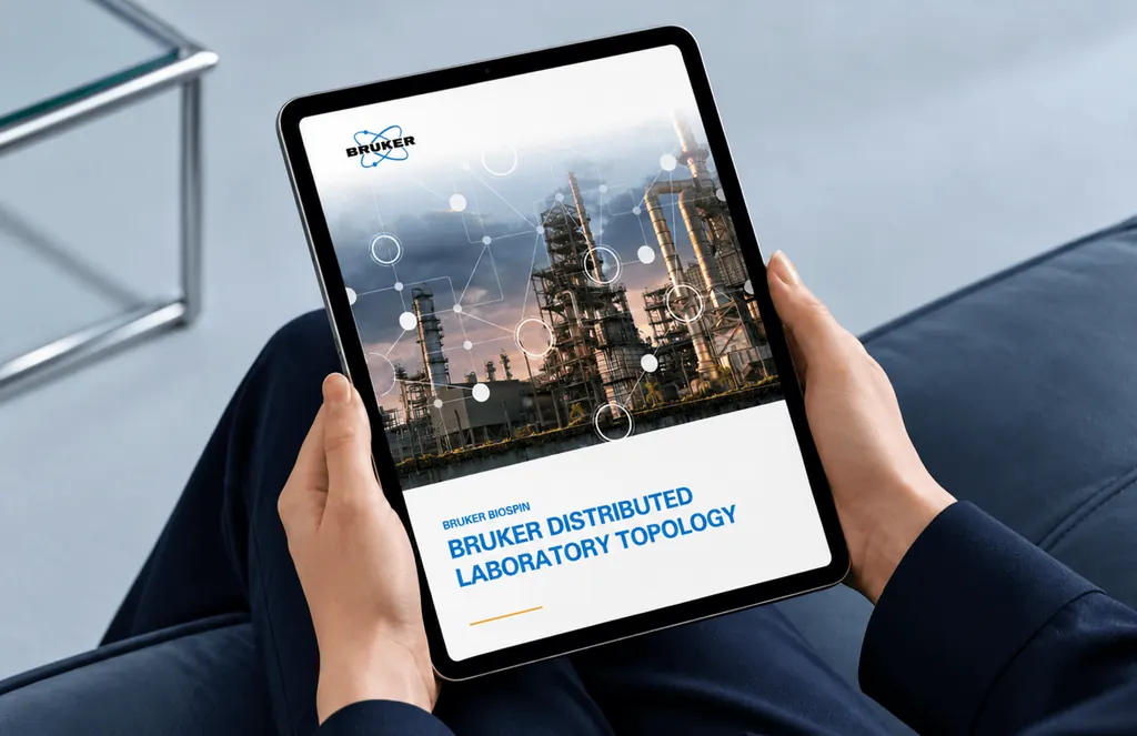 Hands holding a tablet with the Bruker Distributed Laboratory Topology report cover, an industrial plant at dusk