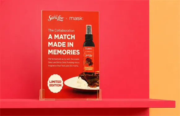 Clear acrylic stand on a red shelf holding a Sara Lee x MaskCo limited edition sign with the spray